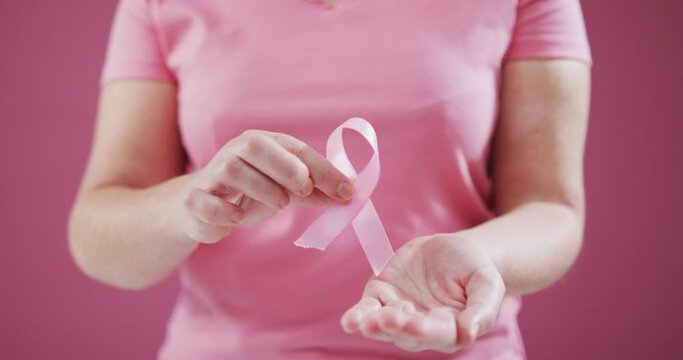 Mid section of woman holding a pink ribbon against pink background