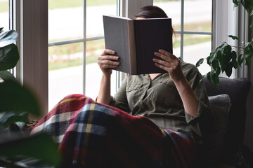 Woman sitting in cozy nook by a window reeding book