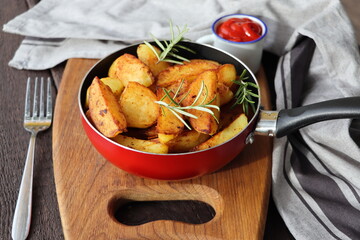 Roasted potatoes with rosemary in iron pan on rustic cutting board