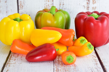 Peppers, variety of colors and sizes, light colored rustic wood background and copy space.