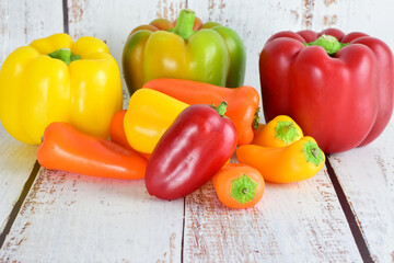 Peppers, variety of colors and sizes, light colored rustic wood background and copy space.