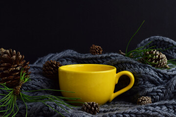Yellow mug, on woolen cloth, pine cones in outline, season, winter concept.