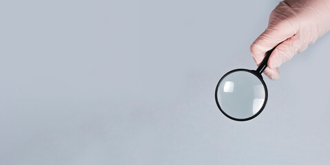 Medical hand in glove with magnifying lens, finding and examining medicine. Banner with copy space...