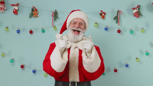 Merry fun old bearded Santa Claus man 50s wears Christmas hat red suit clothes look camera laughing smiling watch comedy movie point finger on you isolated on plain pastel light blue background studio
