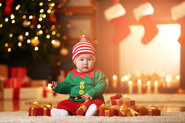 Cute little baby in elf's costume and with gifts at home on Christmas eve