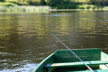 An old wooden, green boat on the river. Fishing rod with a float in the river. Fishing.