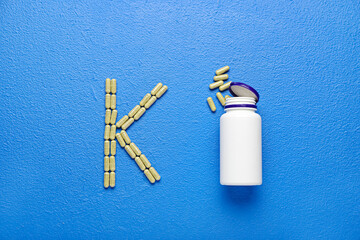 Bottle and letter K made of pills on color background