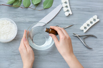 Manicure master adding essential oil to water in bowl on table, top view