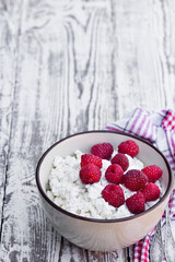 Cottage cheese with raspberry in ceramic bowl on white wooden table