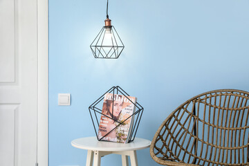 Glowing lamp and table with magazine near blue wall