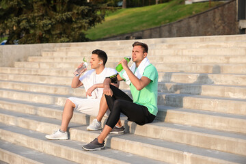 Sporty young men drinking water on stairs outdoors