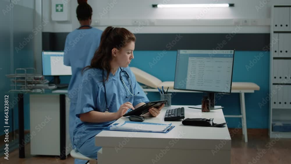 Poster medical assistant typing on tablet screen and checking computer for appointment in doctors office. n
