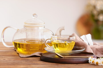 Teapot and cup of fresh chamomile tea on wooden table