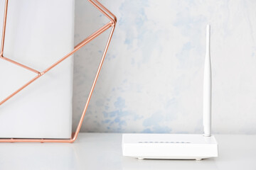 Modern wi-fi router and decor element on table near light wall