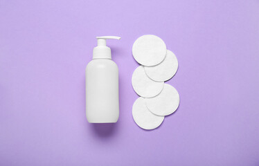 Bottle of cosmetic product and cotton pads on color background