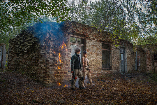 Postapocalyptic biker couple man and woman in grunge militaristic uniforms with weapons against the background of a destroyed brick building.