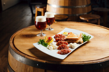 Horizontal photo of beef tartare with mozarella and bread on a wooden table, with two beers at the...