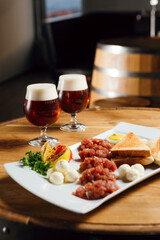 Beef tartare with mozarella and bread on a wooden table, with two beers at the background