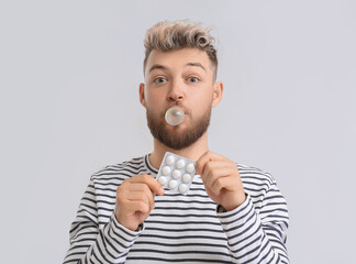 Young man with chewing gum on light background