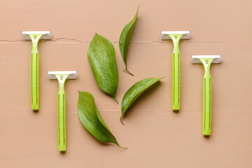 Safety razors and green leaves on color wooden background