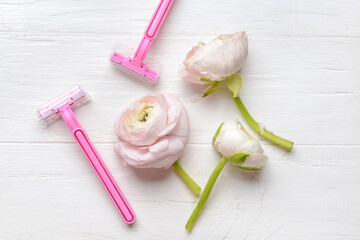Safety razors and flowers on light wooden background