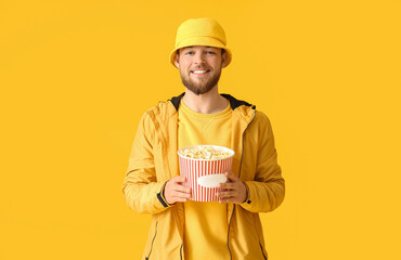 Young man with bucket of popcorn on color background