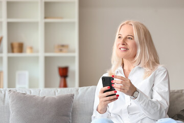 Fototapeta premium Beautiful mature woman using mobile phone at home