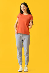 Beautiful teenage girl in orange t-shirt showing thumb-up on yellow background