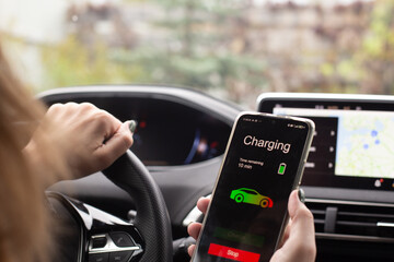 Woman sitting electric car charge using mobile application. Modern technology