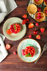 Plates with tasty berry tartlets on wooden background