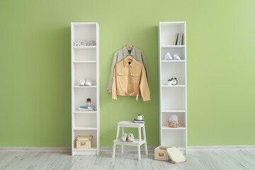 Shelving units and stylish jackets hanging on green wall in hallway
