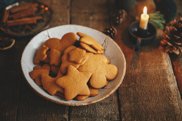 Freshly baked christmas gingerbread cookies in plate on background of rustic table with candle,...