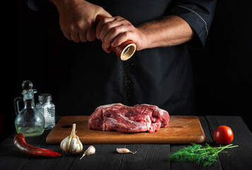 Chef cooking raw meat fillet and adding pepper or chili for marinade on black background. Working environment in kitchen in restaurant or cafe
