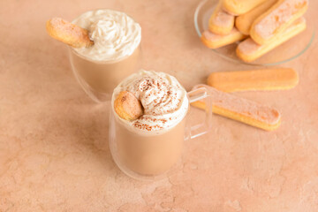 Glass and cup of tasty Tiramisu Latte on beige background