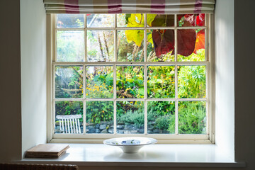 Rustic vintage sash window frame looking out to a lush English country garden with hanging red vine leaves. - obrazy, fototapety, plakaty