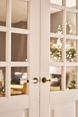 Beautiful modern door knob. Christmas lights on the background. Open, wooden front door from the interior of an upscale home with windows.