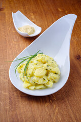 Traditional German potato salad with onion and chives served as close-up in a design bowl on a wooden design board