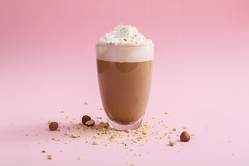 Glass of tasty latte with nuts on pink background