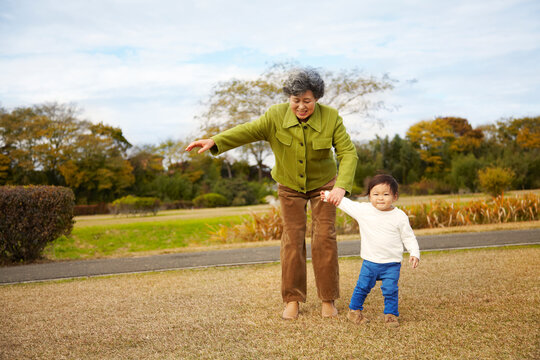 芝生の上で孫の手を引っ張るおばあちゃん