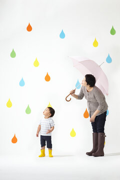 カラフルな雨のしずくバックで虹を見上げるお母さんと子ども