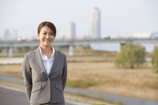 河川敷の土手で笑うフレッシュなビジネスウーマン