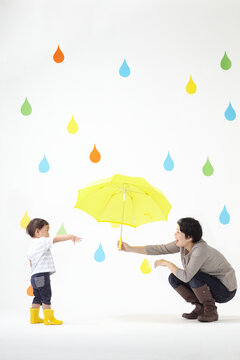 カラフルな雨のしずくマークと黄色い傘を持つママと子ども
