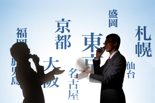 様々な地名の文字の前で電話をしあう男性2人