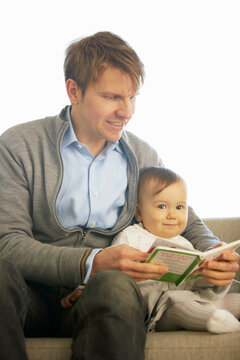ソファーの上で赤ちゃんに絵本を読んであげる父親