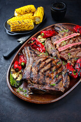 Zwei gegrillte dry aged Wagyu Cote de Boeuf Rindersteaks mit Zucchini und Chili serviert als Draufsicht auf einem rustikalen Design Teller