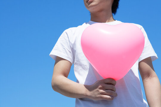 青空にピンクのハートの風船を持つ男性