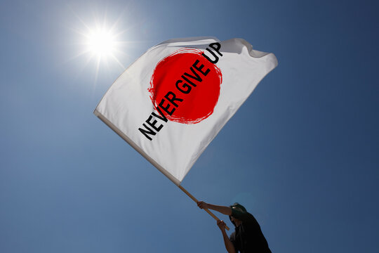 青空と太陽の下でNEVER GIVE UPと書かれた旗を振る男性