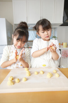 台所で小麦粉を丸くこねてパン作りする女の子の姉妹