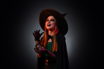 Fototapeta premium Young witch with crystal ball on dark background