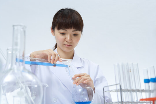 メスシリンダーからフラスコに薬品を移し変える女性研究員